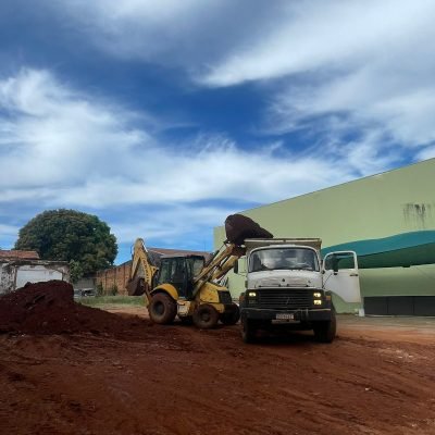 Retroescavadeira realizando o carregamento de terra vermelha na caçamba de caminhão basculante em canteiro de obras regionais.