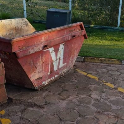Caçamba estacionária vermelha para entulho de obras posicionada em pátio na cidade de Itaí.