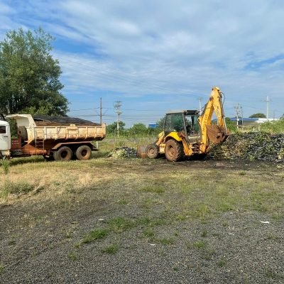 Caminhão basculante branco e retroescavadeira amarela da frota da Mult Lix parados em pátio de obras no interior de SP.