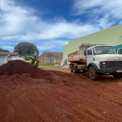 Caminhão basculante branco posicionado ao lado de grande monte de terra vermelha para prestação de serviços de transporte de solo.